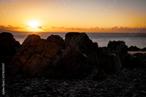 Foto Aerial video along a tropical beach at dawn with golden sunrise over rocks Macka