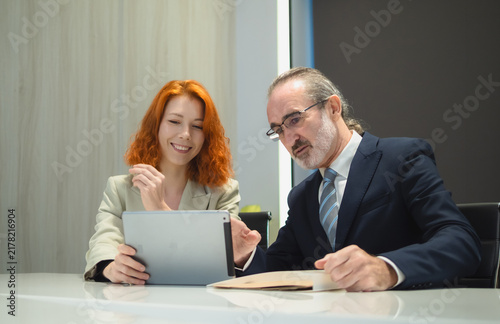 senior male executive explaining a strategic plan with expressive hand gestures to his female colleague holding a digital tablet during a boardroom meeting.