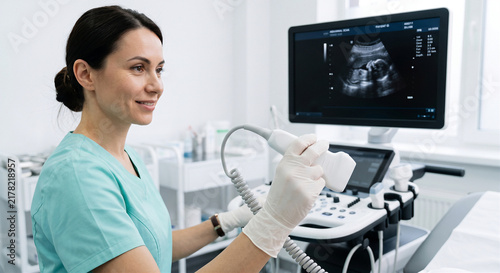 Smiling female sonographer in green scrubs and white gloves performing a fetal ultrasound scan holding the probe.