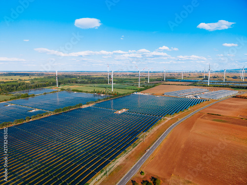 Fotografía Solar panels and wind turbines in a green field landscape