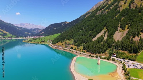 Lake Resia aerial shoreline peninsula surrounding the iconic flooded church steeple in South Tyrol, Italian Alps