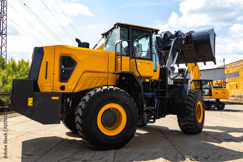 Fototapeta premium Heavy Yellow Wheel Loader with Raised Bucket at Industrial Yard