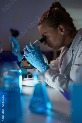 Принти на полотні Female scientist looking into a microscope, conducting research in a dark labora