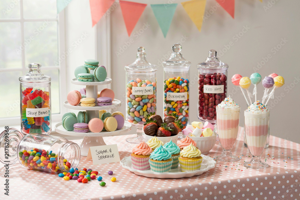 Fototapeta premium Colorful birthday candy buffet table with glass jars and cupcakes birthday cupcakes