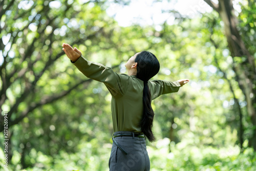 Obraz na plátne Back view of a woman with open arms enjoying fresh air in a sunny green forest, expressing freedom, relaxation and connection with nature