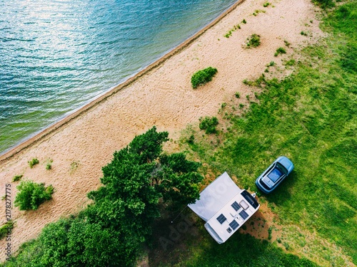 Car parked near water with beach and camper van at lakeside in lush green surroundings