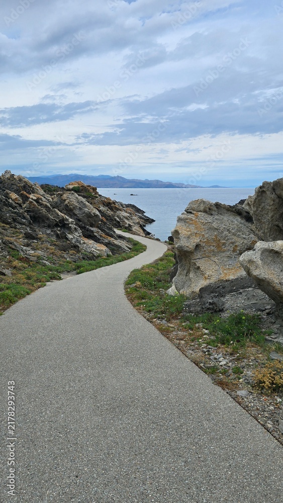Obraz premium Curving coastal asphalt path leading through rocky cliffs near the sea