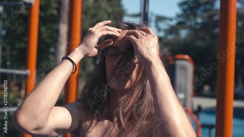 Young athletic man with long hair and glasses at an outdoor gym