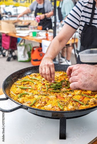 Close-up of hands decorating a large traditional Spanish paella with green peppers during an outdoor culinary festival.