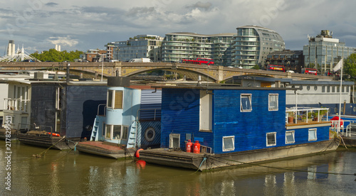 Canvas Print Colorful residential houseboats moored along the River Thames in London, England, with modern high-rise buildings and the city skyline visible in the background