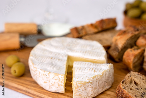 Soft brie cheese on a wooden cutting board, served with rye bread, green olives, and cheese knives. Close-up. Selective focus.