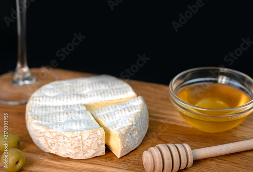 Camembert cheese with honey and olives served with white wine on a wooden board. Creating an elegant appetizer for a dinner, celebration or wine tasting. Close-up. Copy space.
