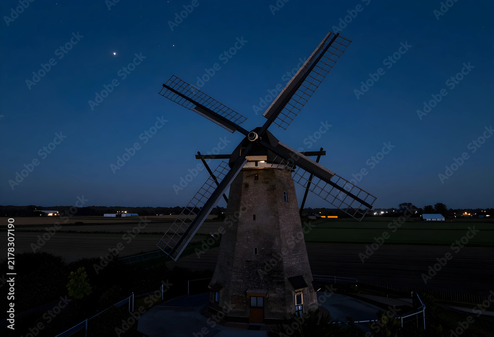 Obraz premium Renewable energy and sustainability, historic windmill in rural landscape at twilight with starry sky and agricultural fields for green power