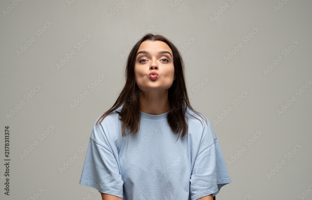 Fototapeta premium Young woman making a kissing face playfully pouting lips in a studio portrait with gray background