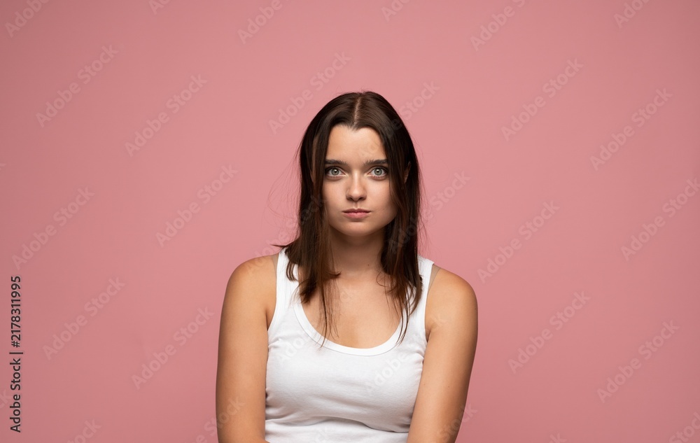 Obraz premium Young woman looking directly at camera with a serious or concerned expression on a pink background, portrait shot