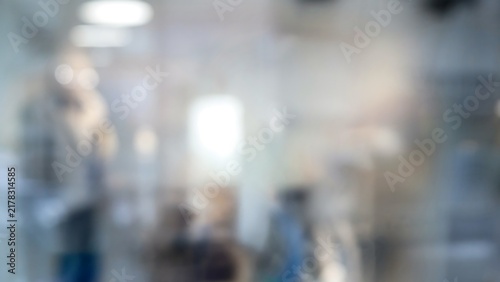 Blurred crowd scene showing people walking in an indoor public space with lighting fixtures visible