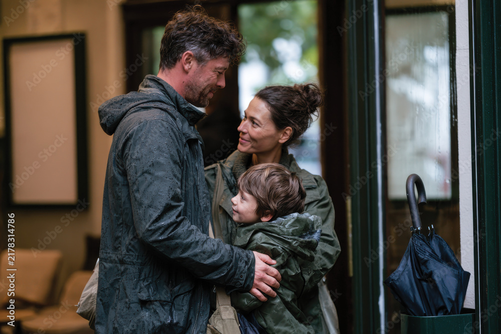 Obraz premium A family shares a joyful embrace outside a building in the rain, capturing a moment of affection and unity amid the elements.