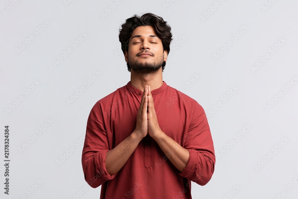 Obraz premium Young man with eyes closed and hands pressed together in a peaceful meditative prayer gesture