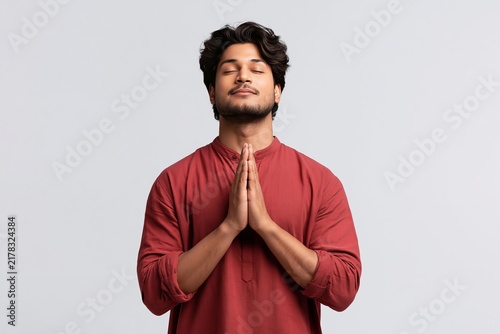 Young man with eyes closed and hands pressed together in a peaceful meditative prayer gesture