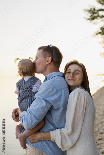 Bild auf Leinwand Loving parents embrace their baby daughter by the water at sunset