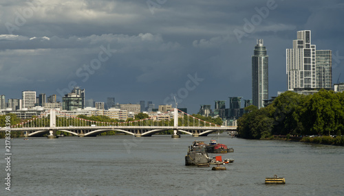 Fotografie Downstream view along the River Thames from Chelsea Embankment in London, featuring river traffic, Grosvenor Railway Bridge and the modern Vauxhall skyline beneath dramatic storm clouds