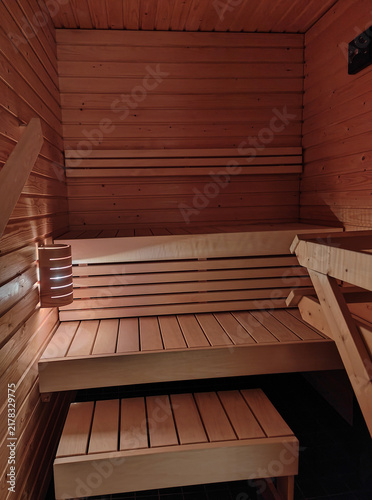 Small wooden sauna interior with tiered benches, timber walls and soft ambient lighting, creating a warm, relaxing wellness and spa atmosphere