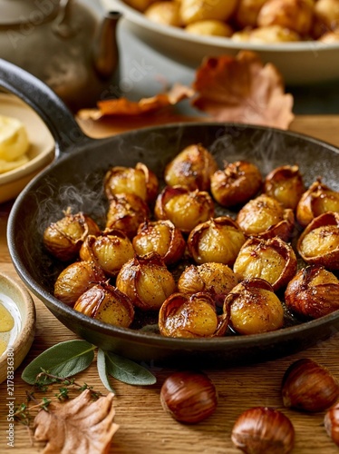 Black cast iron skillet filled with roasted chestnuts. the chestnuts are golden brown and appear to be seasoned with herbs and spices.