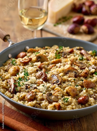 Large frying pan filled with a dish of risotto. the risotto is a creamy yellow color and is topped with small pieces of mushrooms and herbs.