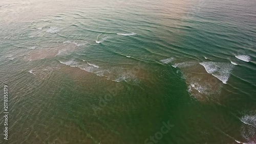 Top down aerial view of the atlantic ocean with beautiful green water and gentle waves washing onto a sandy beach in the algarve region of portugal, creating a tranquil natural background