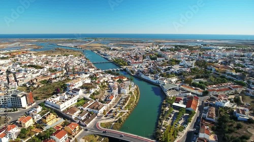 Panoramic aerial footage flying over the gilao river, revealing the historic town of tavira, the ancient roman bridge, and the beautiful algarve coastline under a clear blue sky in portugal