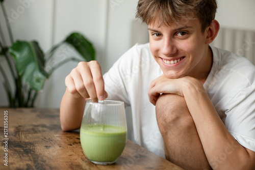 Konstfotografi Happy beautiful teenager looking at camera and mixing fresh green matcha latte d