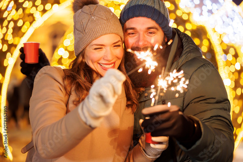 Couple waving with sparklers having fun celebrating New Year outdoors in the city square