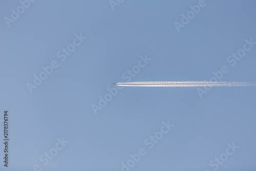 Foto A thin white contrail from an aircraft stretches across a clear light blue sky, viewed from below
