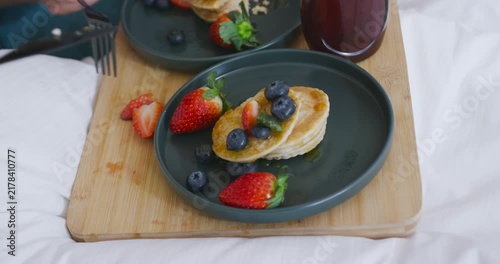 Hand entering from left is cutting pancakes with knife and fork, preparing bite on bed tray