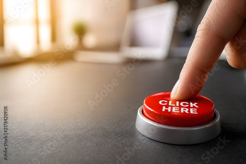 Finger pressing click here button, office workspace background