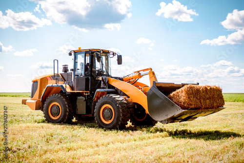 Front loader lifting a hay bale in a field during forage handling and agricultural farm operations.
