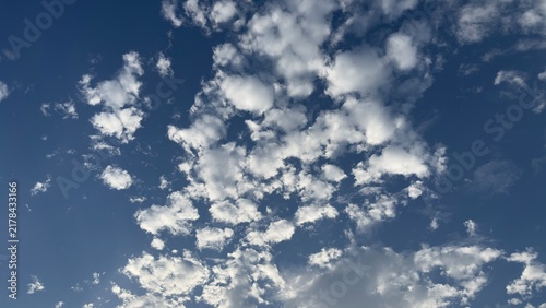 Fotografie Fluffy white cumulus clouds scattered across a clear blue sky on a bright sunny