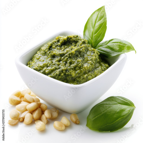pesto sauce in a small white bowl with pine nuts and basil