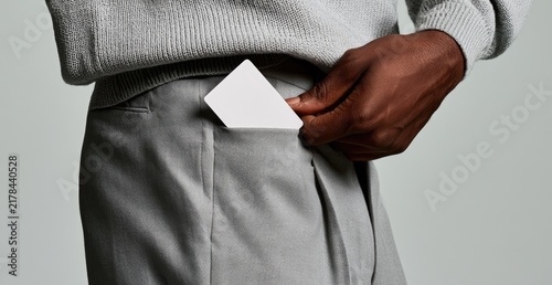 A hand tucks a blank white card into the pocket of gray pants