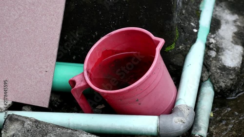 Pink Plastic Mug Filled with Stagnant Water Near PVC Pipes - Dengue Mosquito Breeding Ground, Hygiene Risk, and Sanitation Concept