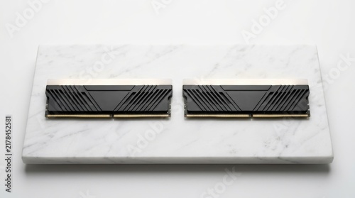 Two black computer RAM memory modules with heatsinks placed neatly on a white marble slab background