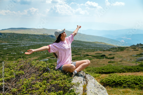 Relaxed woman sitting with open arms high in the summer mountain	