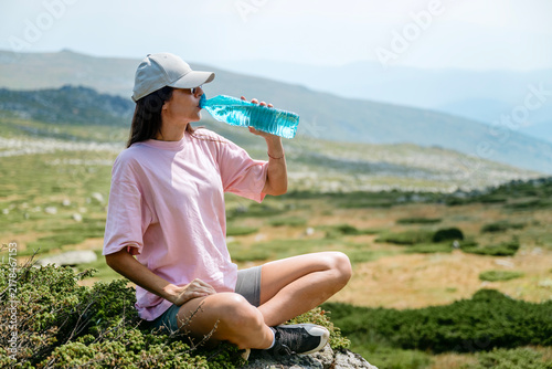 Young hiker woman drinking water in the summer mountain 