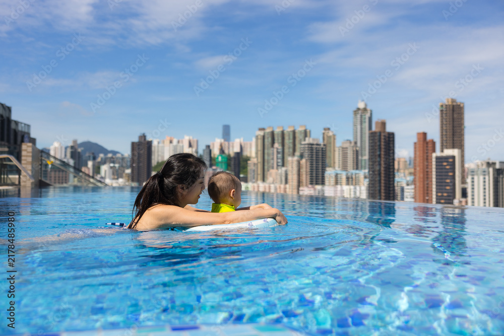 © leungchopan - Mother holding toddler boy in rooftop pool overlooking hong kong city