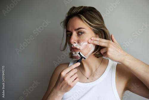 Woman applying facial shaving routine with razor and foam. Beauty, fashion and self-care portrait exploring gender equality, inclusivity, modern grooming habits and contemporary beauty standards