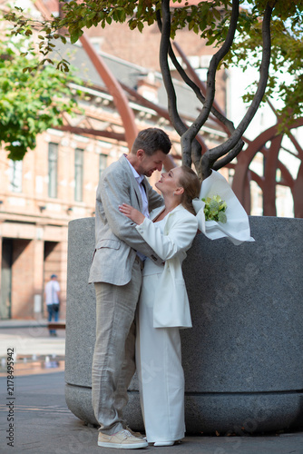 Smiling bride and groom embracing outdoors on wedding day. Emotional romantic moment, modern wedding style, natural light, love and connection between newlyweds.