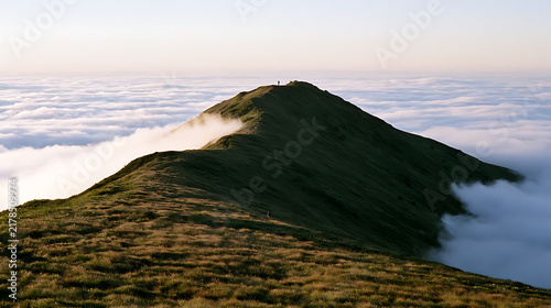 Plakat A solitary traveler stands atop a majestic mountain peak rising proudly above a dense blanket of fluffy white clouds in the early dawn