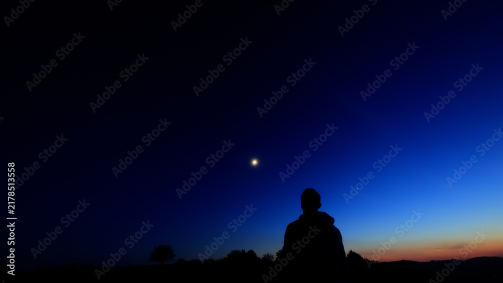 Fototapeta premium Silhouette of a person in nature observing night sky, Moon, stars and planets from a remote location.