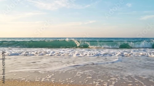 Ocean waves crashing on sandy beach with foamy water rolling towards shore under blue sky with beach white foam rolling onto video ocean waterfront coastline landscape