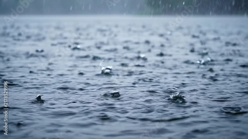 Heavy rain falling on the surface of a dark lake with creating continuous ripples small water splashes falling onto video heavy precipitation environment atmospheric